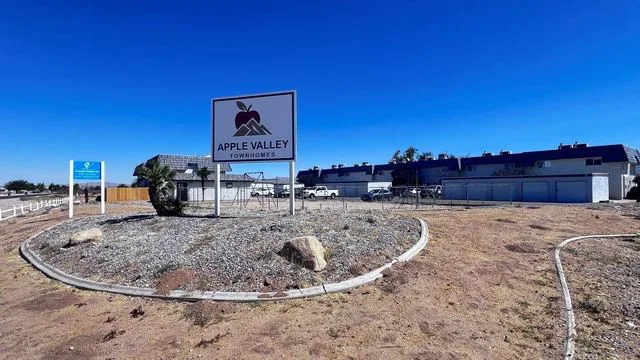 The Apple Valley Townhomes sign at the entrance, the apple and mountain logo on a white panel against a deep blue sky