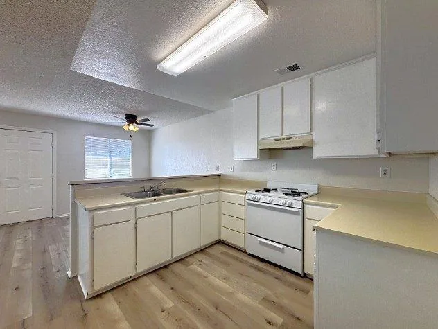 A renovated kitchen with white cabinets, a white gas range and light wood-look flooring