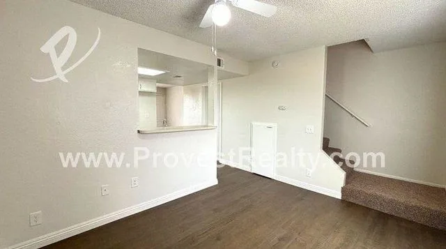 The living room of a two-story townhome, wood-look flooring and the carpeted stairs going up to the bedrooms
